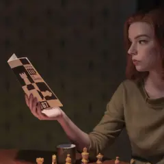 Beth Harmon studiert eine Schachpartie, inspiriert vom Damengambit. Schachfiguren und eine Tasse stehen auf dem Tisch.