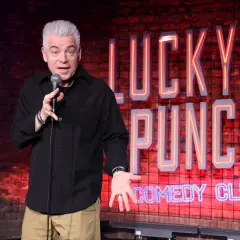 Ein Comedian mit grauem Haar steht auf der Bühne des "Lucky Punch Comedy Club" und erzählt Witze.