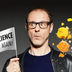 Vince Ebert mit Brille hält eine Fahne "Make Science Great Again!". Er blickt überrascht auf zerbrechende Macarons und eine Löwenzeichnung.