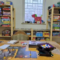 Regale voller Brettspiele für sprachspiele erwachsene. Ein Spielbrett mit Figuren liegt auf dem Tisch.