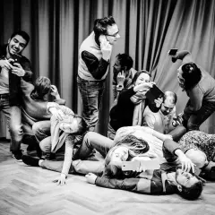 Eine Gruppe von Menschen, die scheinbar **theater spielen**, hält Handys und Tablets. Manche telefonieren, andere machen Selfies.