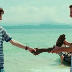 Besetzung von Call Me By Your Name: Elio und Oliver am See, Oliver hält eine Statue.