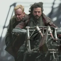 Zwei Männer auf einem Motorrad in der Serie "Andor". Der Fahrer blickt entschlossen, der Beifahrer besorgt.