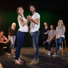Ein Paar tanzt im Scheinwerferlicht, während andere Teilnehmer eines Improvisationstheater Kurses im Hintergrund sitzen und zuschauen.