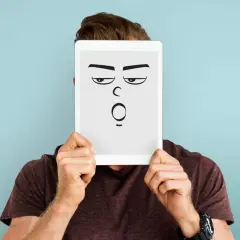 Mann hält Tablet mit cartoonhaftem Gesicht, das genervt und überrascht schaut. Perfekt für die sarkasmus definition.