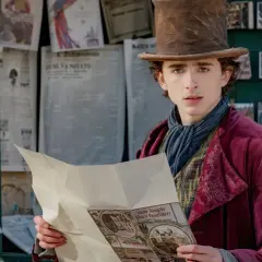 Timothée Chalamet als junger Willy Wonka, der in einem viktorianischen Outfit und mit einem Zylinder vor einem Zeitungskiosk steht und eine Broschüre liest. Die Besetzung von Wonka verspricht Magie.