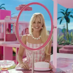 Margot Robbie als Barbie im Film, lächelnd durch einen pinken Spiegel, umgeben von einer rosafarbenen Traumwelt.