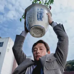 Ein Mann hält einen Blumentopf über seinem Kopf. Wasser tropft herunter. Eine Szene aus dem Film "No other choice".