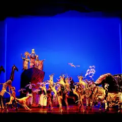 Bühnenszene mit Darstellern in Tierkostümen und Figuren, die den Beginn eines Musicals in Deutschland feiern.