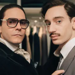 Zwei Männer in eleganter Kleidung, einer mit Brille und Krawatte, der andere mit Schnurrbart, scheinen auf dem Weg zu sein, Karl Lagerfeld zu werden.