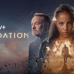 Apple TV+ "Foundation" Serie: Drei Hauptfiguren blicken ernst in die Ferne, während ein Mann im Vordergrund eine Hand ausstreckt.