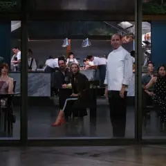 Gäste in einem schicken Restaurant blicken schockiert auf den Koch, der das Menü präsentiert.