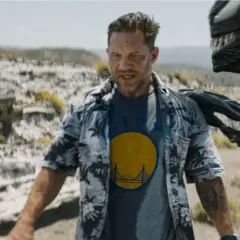 Tom Hardy als Eddie Brock, mit Venom, der sich hinter ihm im Ödland windet. Ein Blick auf die Besetzung von Venom: The Last Dance.