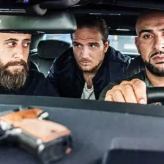 Drei Männer, die wie 4 Blocks Schauspieler aussehen, sitzen in einem Auto. Eine Pistole liegt auf dem Armaturenbrett.