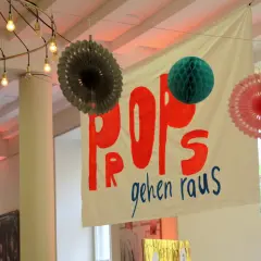 Bunte Papier-Props und eine Fahne mit der Aufschrift "POPS gehen raus" hängen von der Decke.