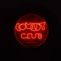 Rotes Neonschild "COMEDY CLUB" im Dunkeln. Ein Ort, an dem die Bedeutung von Kabarett durch Lachen und Unterhaltung lebendig wird.