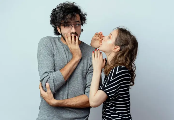 Sie flüstert ihm etwas ins Ohr, sein Gesichtsausdruck deutet auf ein **double entendre** hin.
