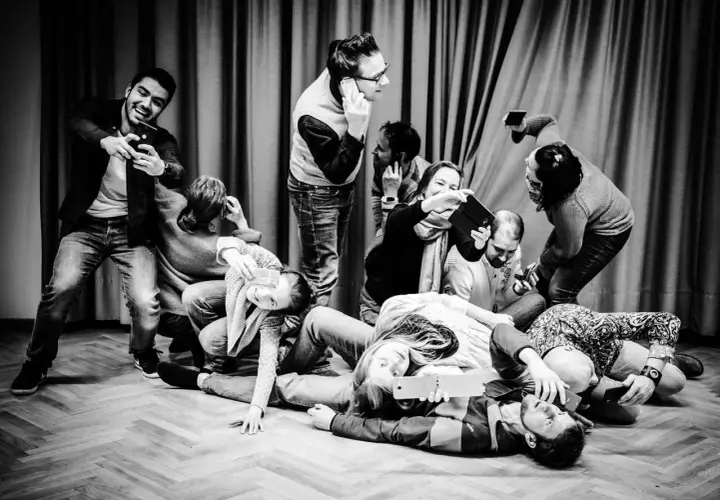 Eine Gruppe von Menschen, die scheinbar **theater spielen**, hält Handys und Tablets. Manche telefonieren, andere machen Selfies.