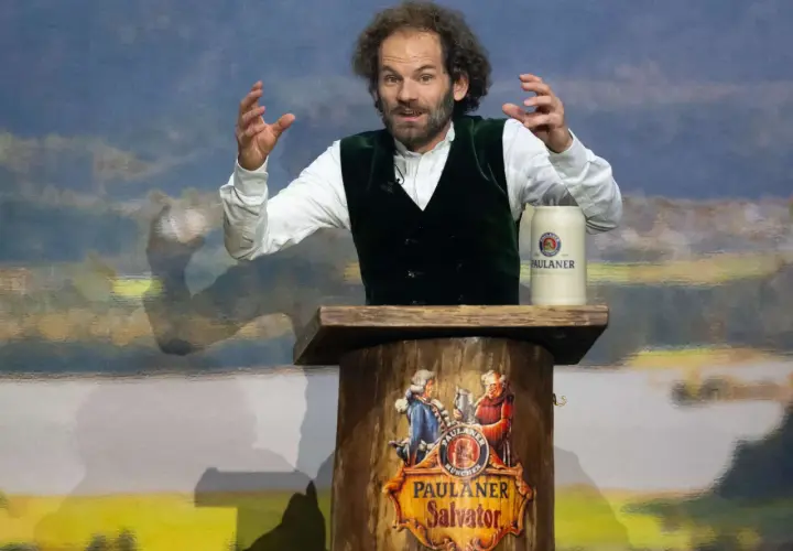 Ein Mann mit Lockenmähne und grünen Weste hält eine Rede am Nockherberg. Seine Gestik und Mimik lassen auf eine kritische Auseinandersetzung schließen.