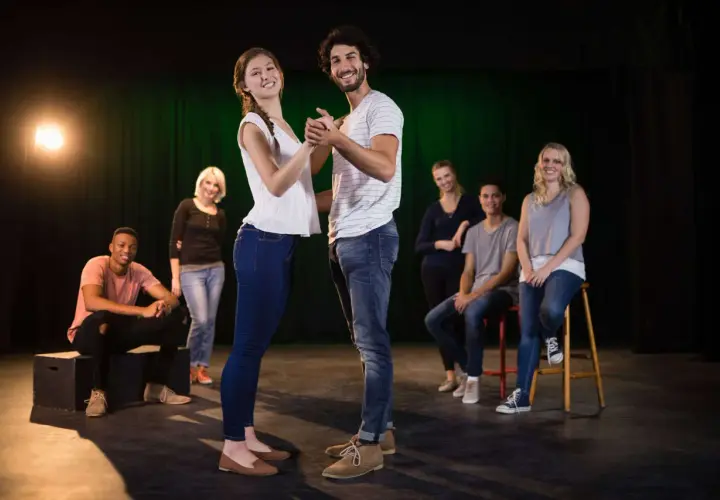 Ein Paar tanzt im Scheinwerferlicht, während andere Teilnehmer eines Improvisationstheater Kurses im Hintergrund sitzen und zuschauen.