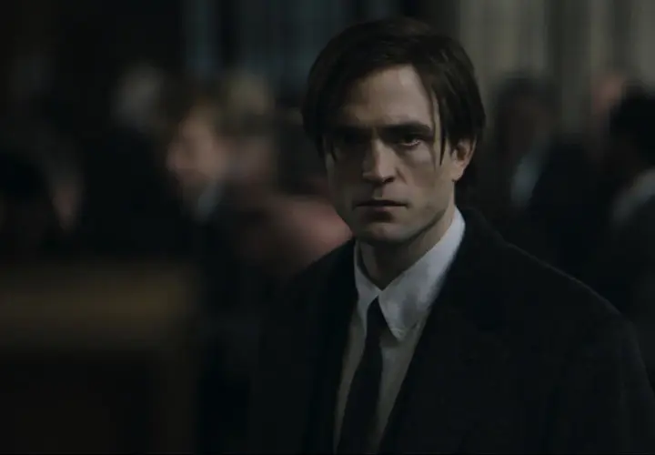 Robert Pattinson als der junge Batman, mit ernstem Blick und dunklem Anzug, inmitten einer Menge.
