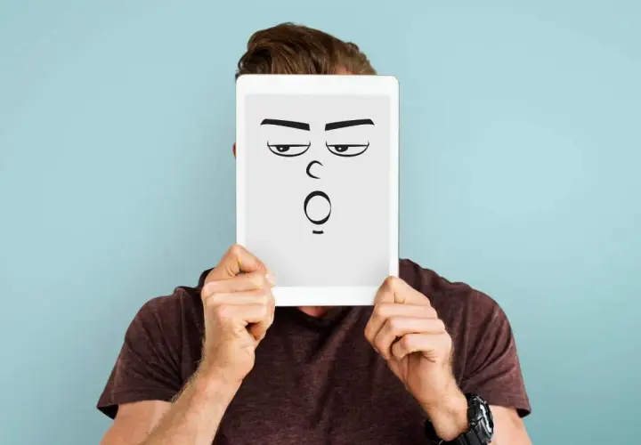 Mann hält Tablet mit cartoonhaftem Gesicht, das genervt und überrascht schaut. Perfekt für die sarkasmus definition.