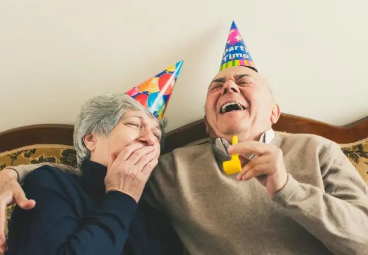 Ein älteres Paar mit Partyhüten lacht herzhaft. Sie zeigen, wie man jemanden zum Lachen bringt: mit Freude und Humor.