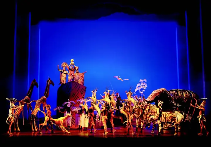 Bühnenszene mit Darstellern in Tierkostümen und Figuren, die den Beginn eines Musicals in Deutschland feiern.