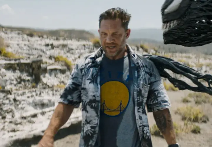 Tom Hardy als Eddie Brock, mit Venom, der sich hinter ihm im Ödland windet. Ein Blick auf die Besetzung von Venom: The Last Dance.