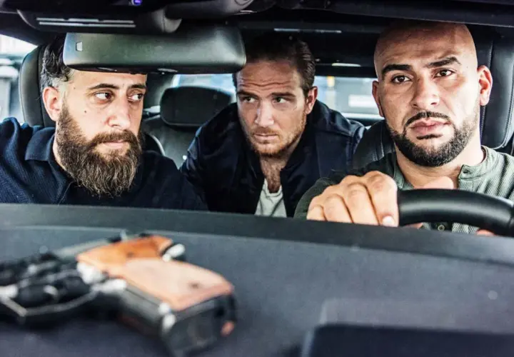 Drei Männer, die wie 4 Blocks Schauspieler aussehen, sitzen in einem Auto. Eine Pistole liegt auf dem Armaturenbrett.