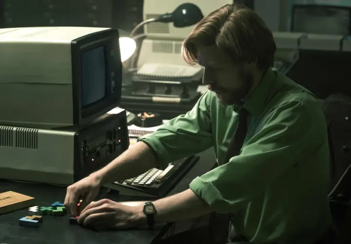 Mann mit Bart spielt mit Tetris-Steinen vor einem alten Computer. Ein Moment aus dem "Tetris"-Film.