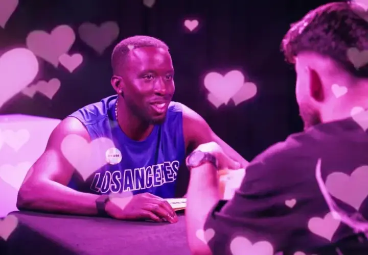 Zwei Männer im Gespräch, umgeben von rosa Herzen. Einer trägt ein blaues Tanktop mit "Los Angeles". Der Vibe ist wie ein "roasted jugendsprache" Date.