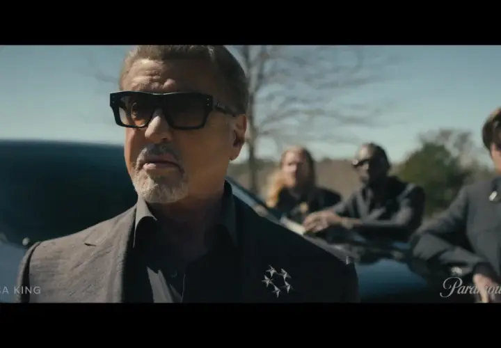 Sylvester Stallone als Tulsa King, mit Sonnenbrille und Anzug, steht vor einem Auto, begleitet von drei Männern.
