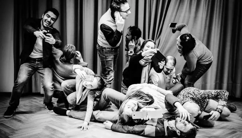Eine Gruppe von Menschen, die scheinbar **theater spielen**, hält Handys und Tablets. Manche telefonieren, andere machen Selfies.
