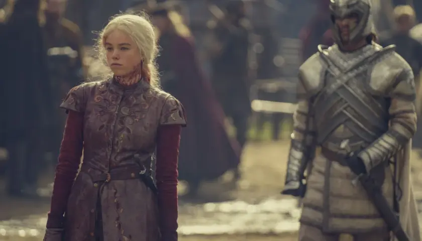 Rhaenyra Targaryen, blutverschmiert, blickt nachdenklich, während ein Ritter in voller Rüstung im Hintergrund der Folgen von House of the Dragon steht.