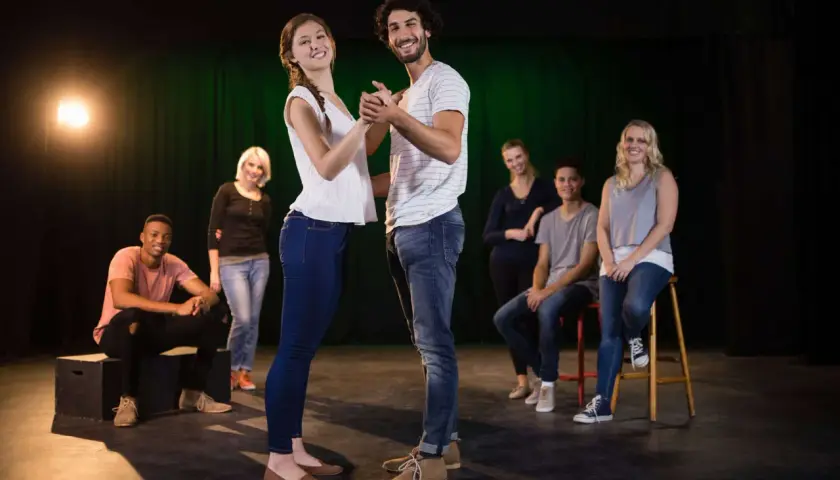 Ein Paar tanzt im Scheinwerferlicht, während andere Teilnehmer eines Improvisationstheater Kurses im Hintergrund sitzen und zuschauen.