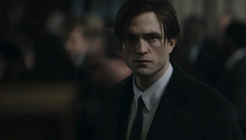 Robert Pattinson als der junge Batman, mit ernstem Blick und dunklem Anzug, inmitten einer Menge.