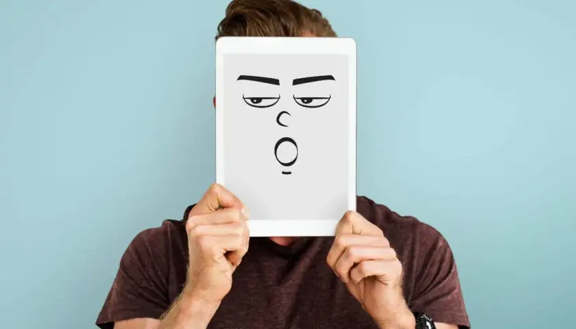 Mann hält Tablet mit cartoonhaftem Gesicht, das genervt und überrascht schaut. Perfekt für die sarkasmus definition.