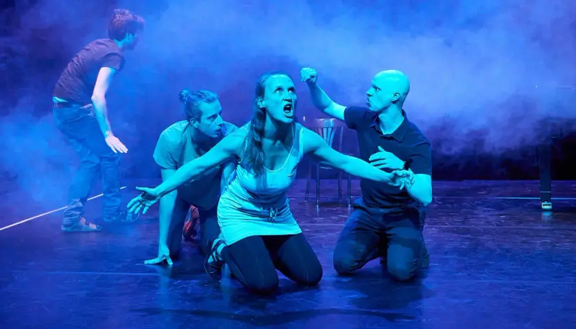 Dramatische Szene mit vier Darstellern auf einer Bühne. Eine Frau schreit, umgeben von drei Männern. Typische Merkmale eines Musicals: Emotion, Bewegung und Inszenierung.