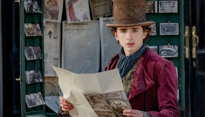 Timothée Chalamet als junger Willy Wonka, der in einem viktorianischen Outfit und mit einem Zylinder vor einem Zeitungskiosk steht und eine Broschüre liest. Die Besetzung von Wonka verspricht Magie.