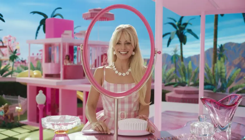 Margot Robbie als Barbie im Film, lächelnd durch einen pinken Spiegel, umgeben von einer rosafarbenen Traumwelt.