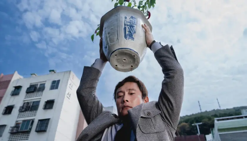 Ein Mann hält einen Blumentopf über seinem Kopf. Wasser tropft herunter. Eine Szene aus dem Film "No other choice".