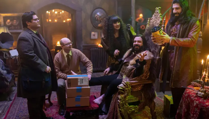Die Besetzung von "What We Do in the Shadows" in einem opulenten Raum. Nandor sitzt auf einem Thron, während Nadja und Laszlo daneben stehen. Guillermo und Colin Robinson sind ebenfalls anwesend.