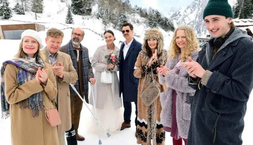 Die besetzung von der spitzname feiert eine Hochzeit im Schnee. Eine Braut mit Blumenstrauß, ein Bräutigam mit Schnurrbart und Gäste in Wintermänteln.