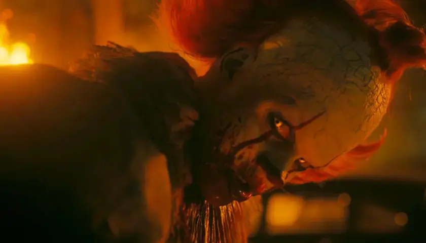 Pennywise, der Clown, blickt mit leuchtenden Augen aus dem Feuer. Willkommen in Derry, wo er auf seine Opfer wartet.