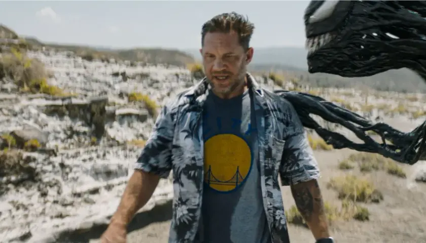 Tom Hardy als Eddie Brock, mit Venom, der sich hinter ihm im Ödland windet. Ein Blick auf die Besetzung von Venom: The Last Dance.