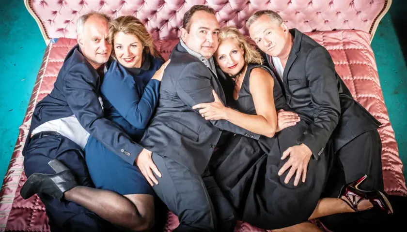 Fünf Personen, eng umschlungen auf einem rosa Bett. Eine Szene, die an ein **hidden Shakespeare**-Drama erinnert, voller Leidenschaft und Geheimnisse.