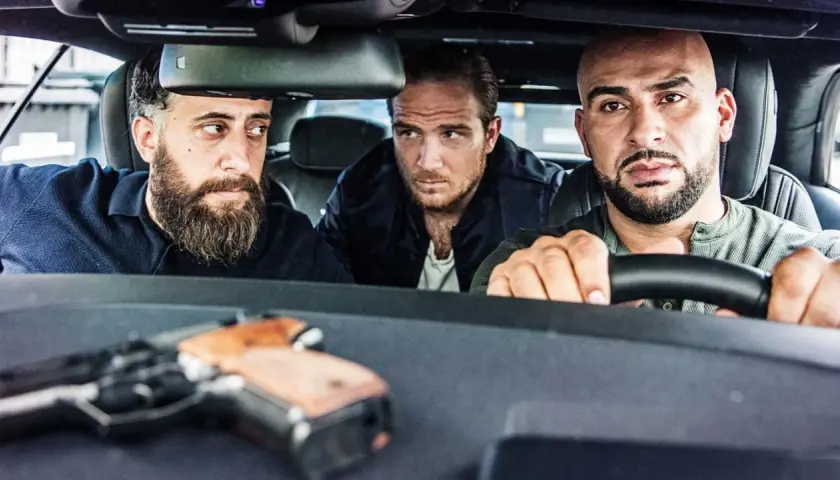 Drei Männer, die wie 4 Blocks Schauspieler aussehen, sitzen in einem Auto. Eine Pistole liegt auf dem Armaturenbrett.