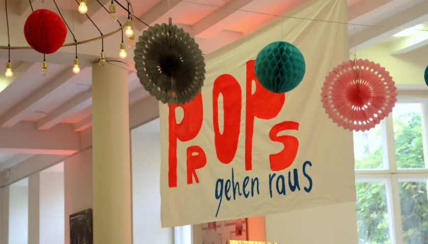 Bunte Papier-Props und eine Fahne mit der Aufschrift "POPS gehen raus" hängen von der Decke.