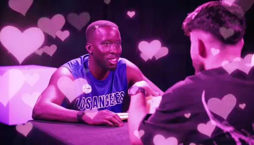 Zwei Männer im Gespräch, umgeben von rosa Herzen. Einer trägt ein blaues Tanktop mit "Los Angeles". Der Vibe ist wie ein "roasted jugendsprache" Date.